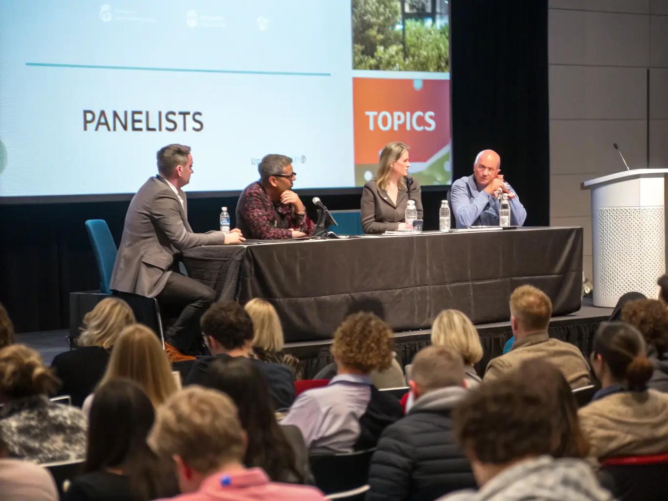 A photograph of a panel discussion at a tech conference, featuring diverse speakers and an engaged audience, with the Canadian flag subtly displayed in the background.